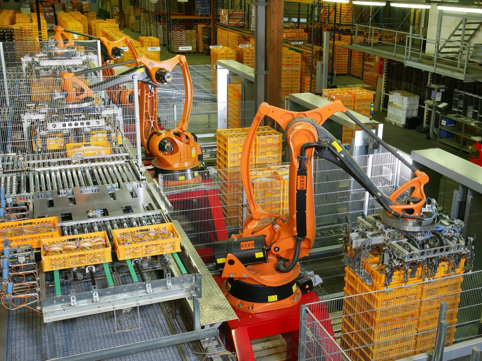 Orange industrial robot arms handling bakery crates inside a factory.